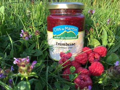 Pot de confiture de framboises, placé dans l'herbe avec des framboises fraîches sur le côté.