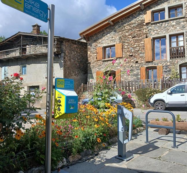 Bornes de recharge vélos électriques avec maison en pierres en arrière plan