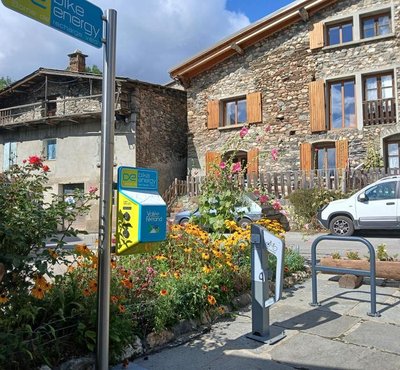 Bornes de recharge vélos électriques avec maison en pierres en arrière plan