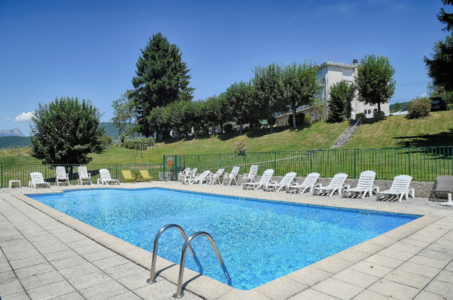 Piscine extérieure rectangulaire, entourée de chaises longues et d'une terrasse ensoleillée.