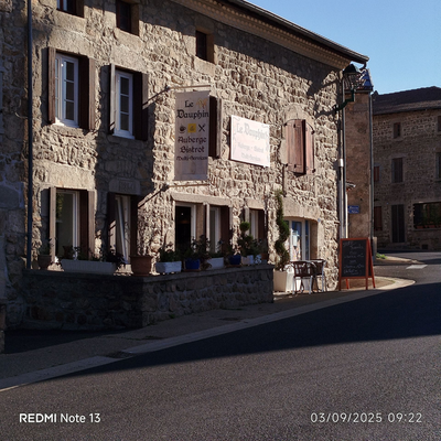 Une petite terrasse fleurie vous accueille avec une pancarte et un oriflamme identifiant l'auberge