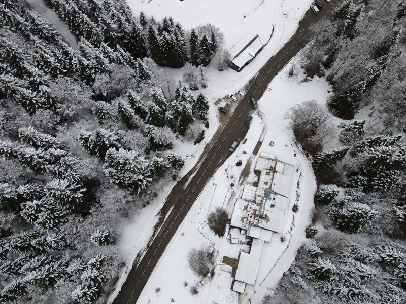 Vue drone du gîte et auberge de Carri à La Chapelle en Vercors, avec la route enneigée qui serpente à travers une forêt [...]